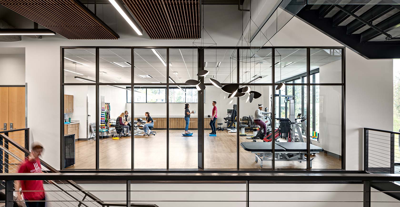 Students work in a rehabilitation classroom, seen through large interior windows beyond an open stairwell.