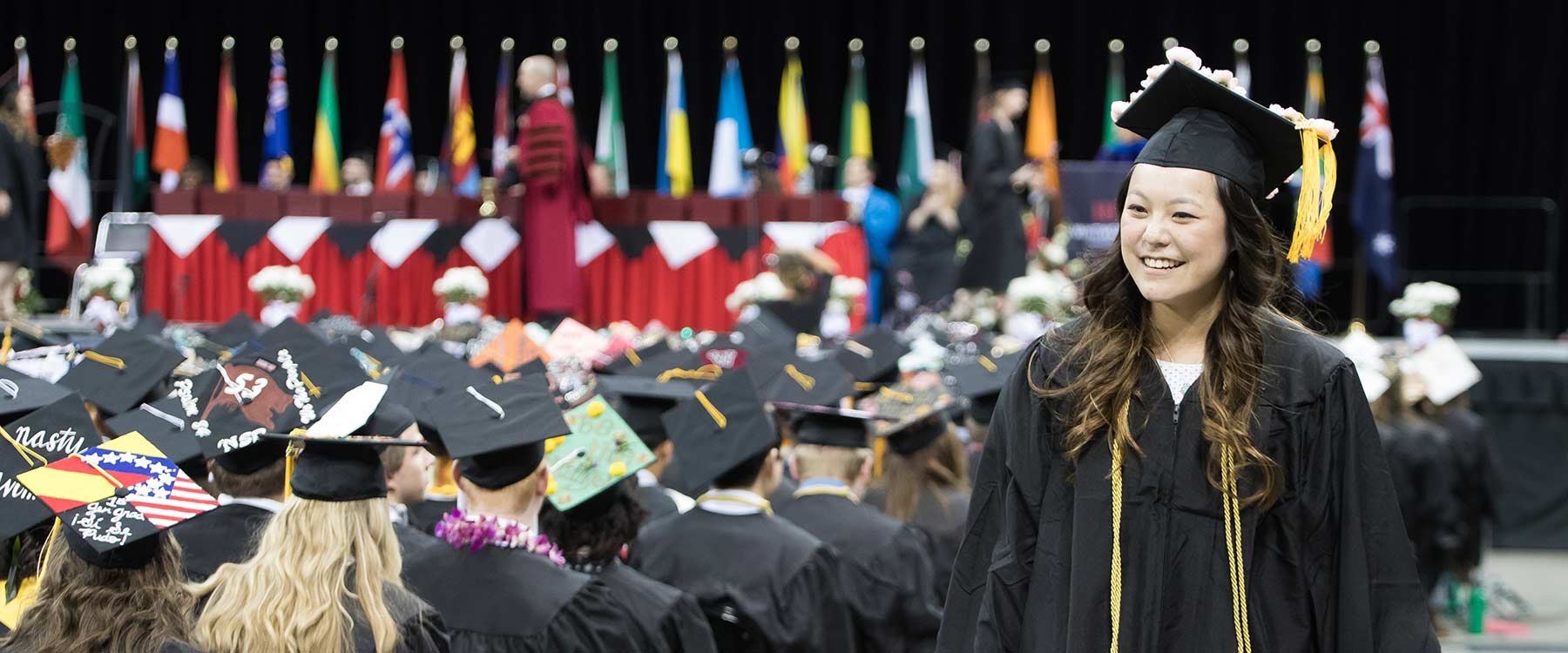 A student in a cap and gown walks past rows of other graduates during commencement.