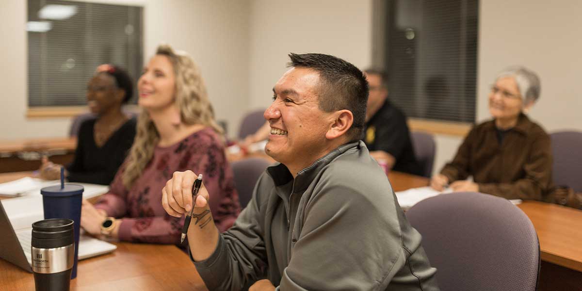 A group of adults smiling and listening attentively in a classroom setting.