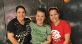 Three students smiling and sitting close together in front of a colorful, abstract background.