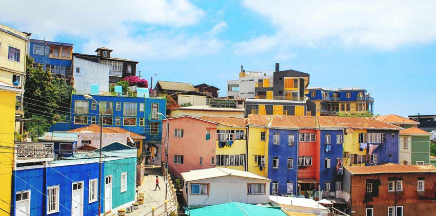 A vibrant neighborhood with colorful buildings on a sunny day under a blue sky with scattered clouds.