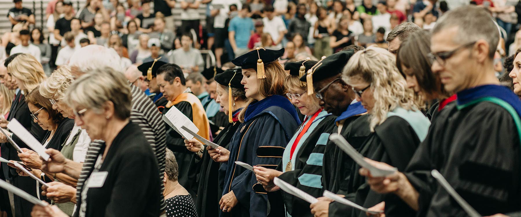 Faculty in regalia stand together in a crowd at a university convocation ceremony.
