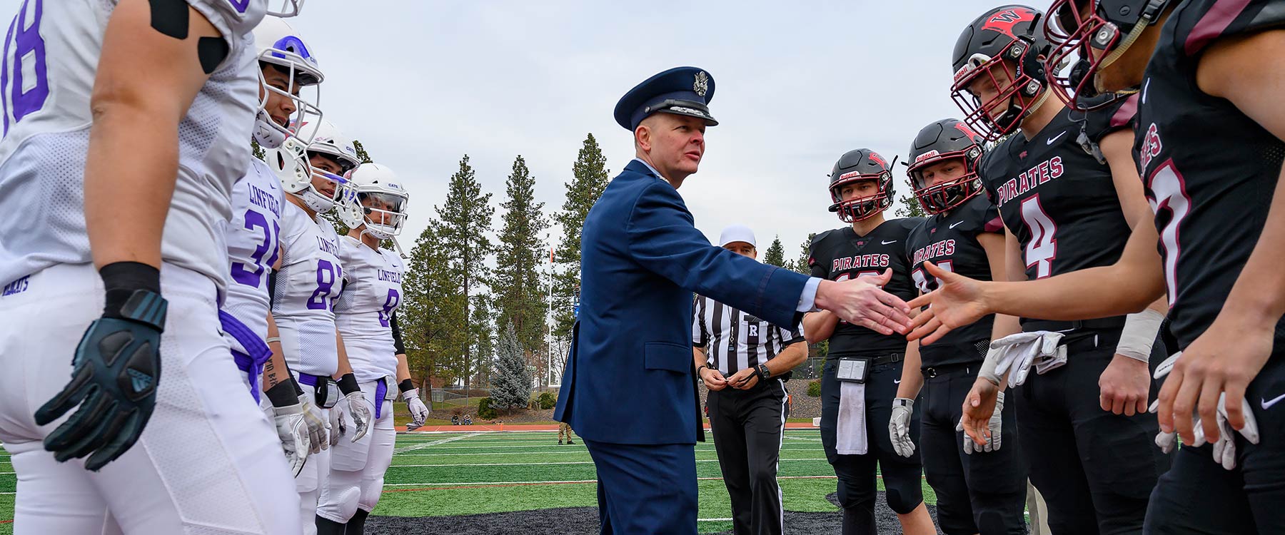 An officer in uniform shakes the hand of a Whitworth football player on the field.