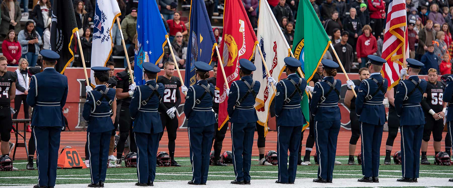 People in uniform salute flags