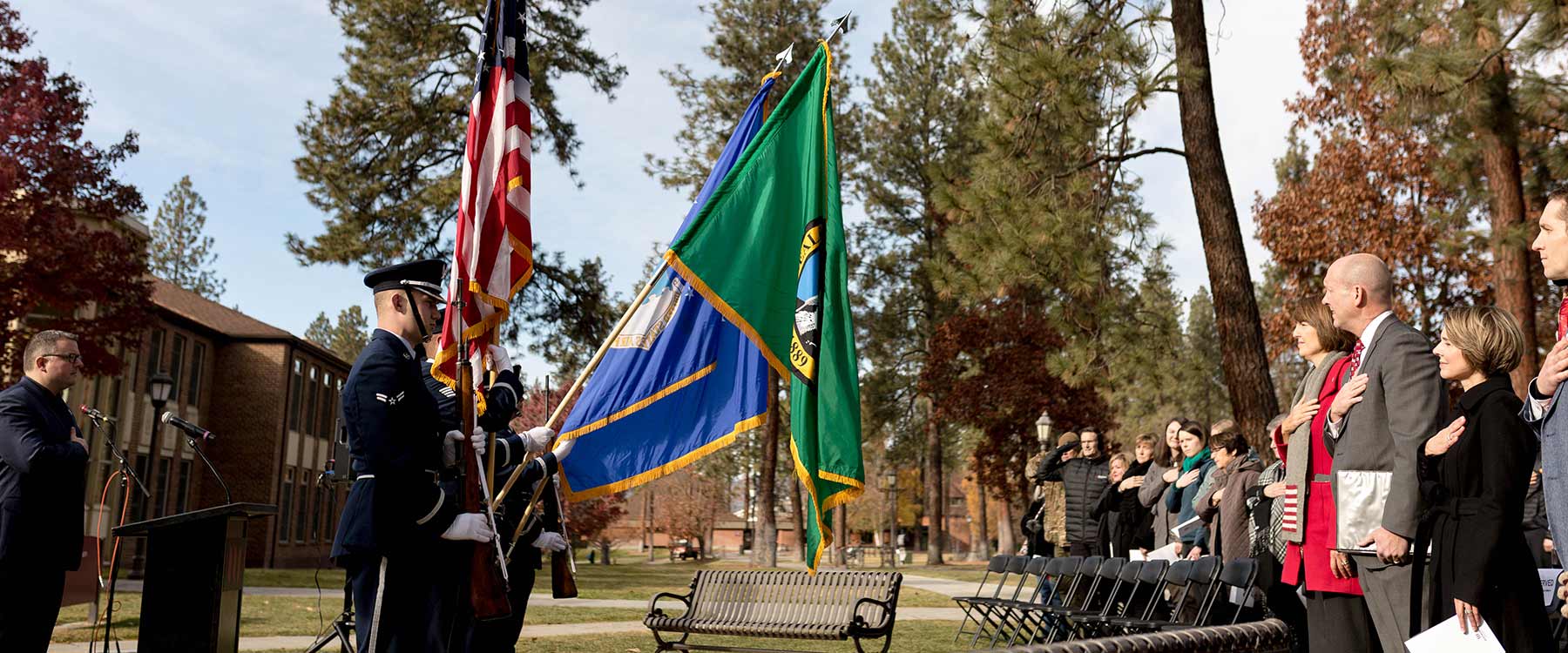 A crowd puts their hands over their hearts as they look at flags
