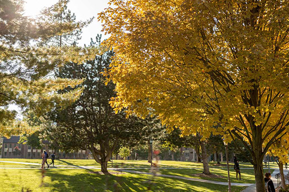 A maple tree with autumn colored leaves and students walking to classes on Whitworth campus in the fall. 