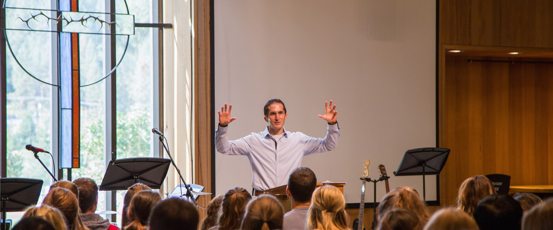 Forrest Buckner stands at the front of the chapel, speaking to a group of seated students.