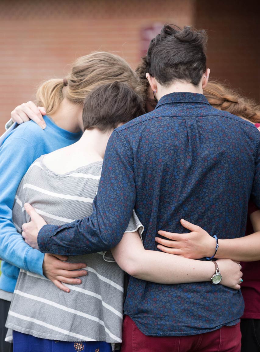 Students gather in a tight circle and bow their heads together.