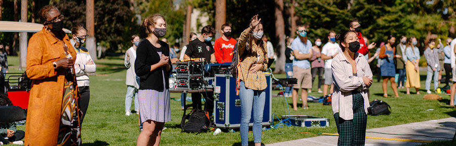 Students sing and take part in an outdoor chapel event on campus. All are wearing masks.