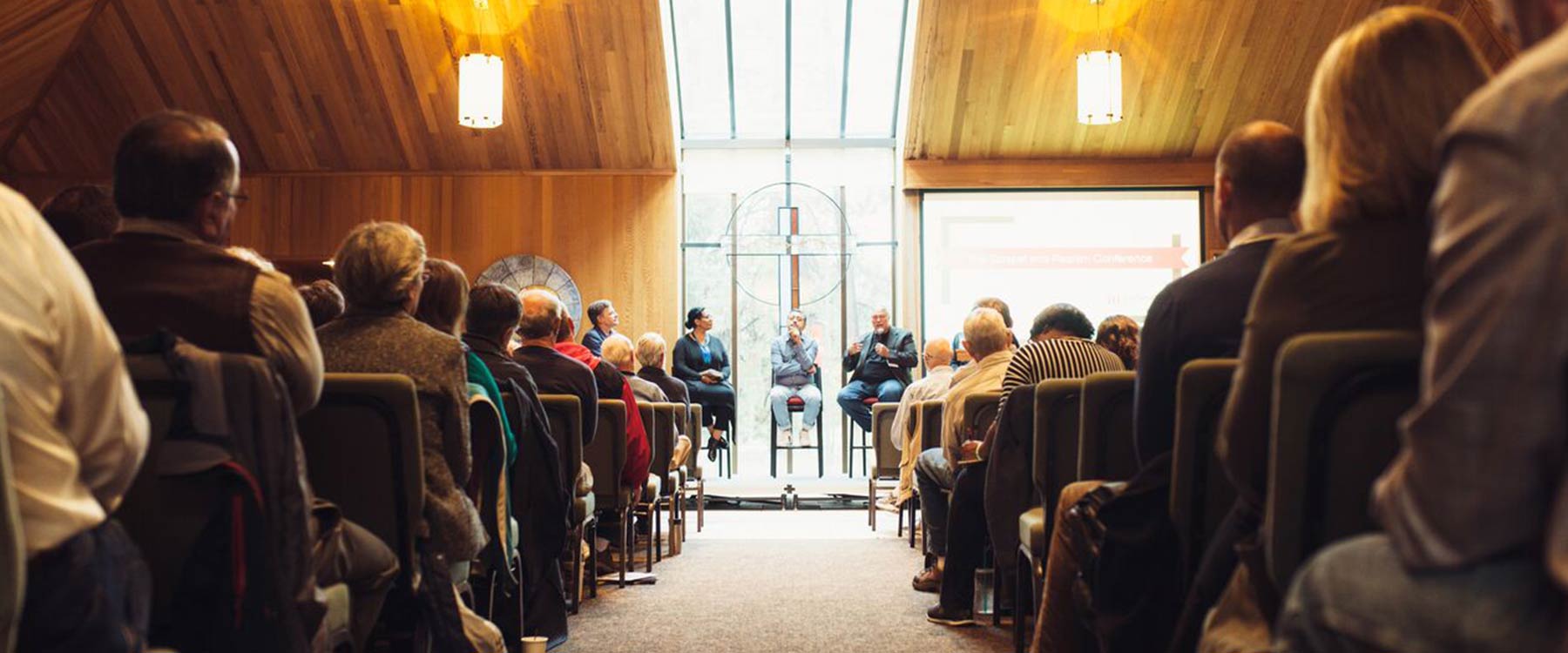 A panel of speakers sits at the front of the university chapel. The rows of seats are filled with listeners.