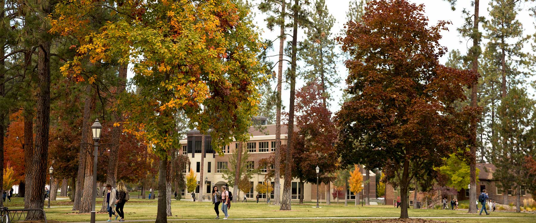 The Whitworth campus in fall, with colorful trees, students walking, and a stately academic building in the background.