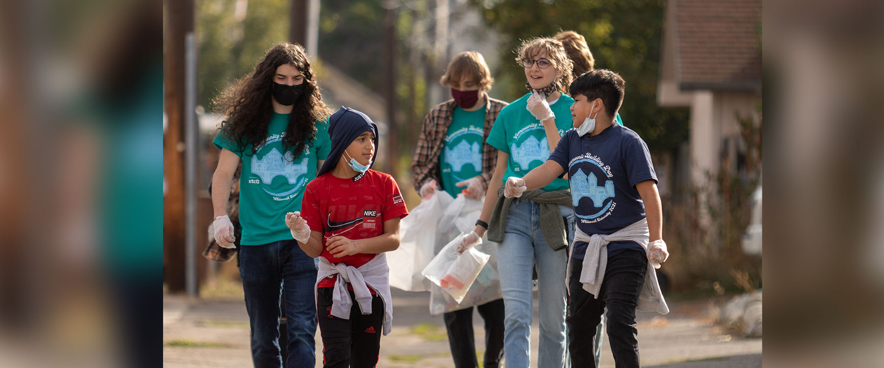 A group of young volunteers walk together outdoors, wearing gloves and carrying trash bags during a cleanup event.