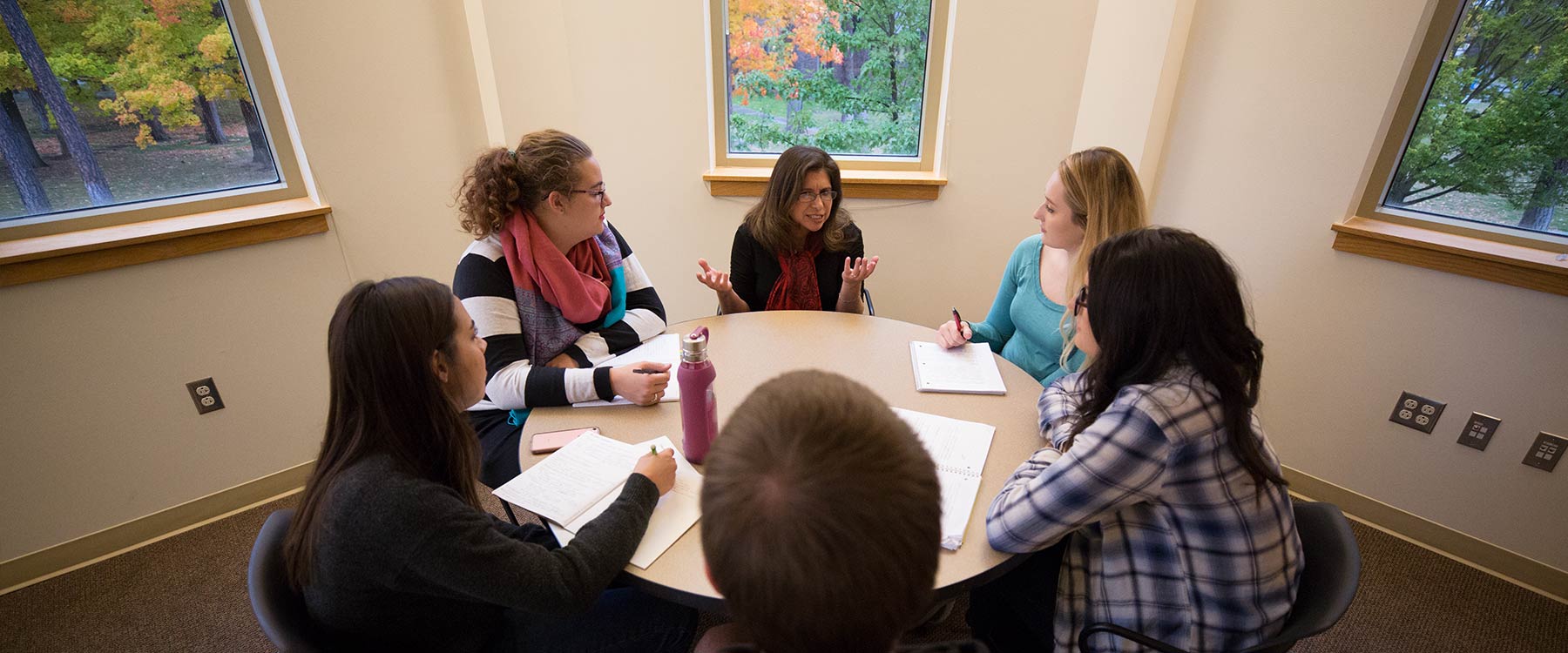 Five students sit around a small table with a professor who is engaged in an animated presentation.