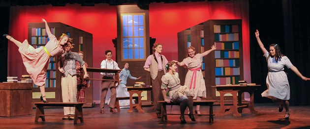 Multiple student actors dance on a brightly-colored stage in a theatre production.