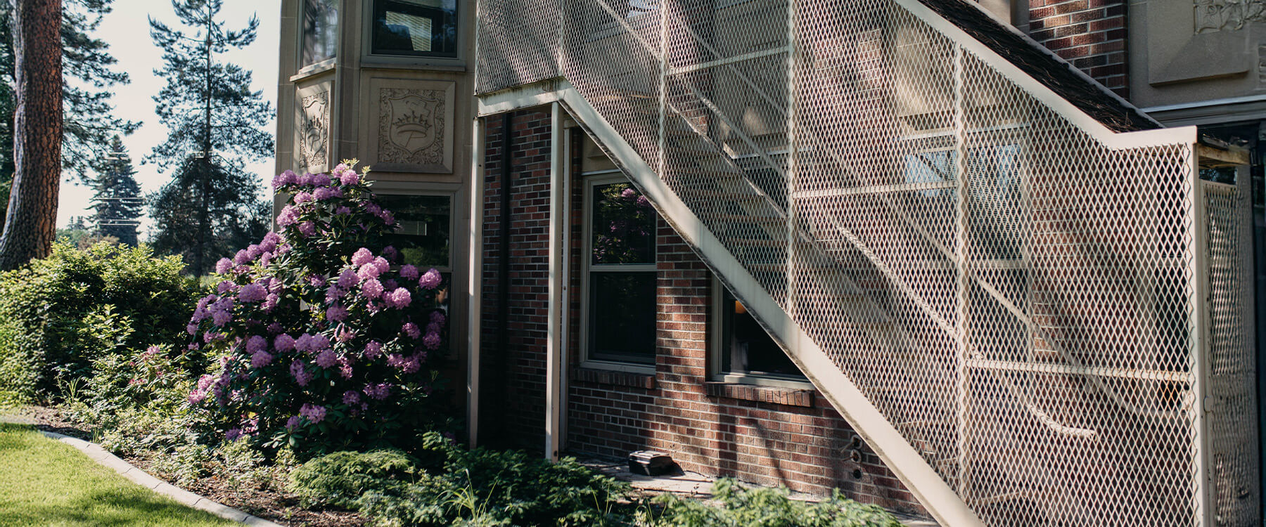 A student sits on a ledge outside of Weyerhaeuser Hall and highlights a textbook. Three students walk toward the building.