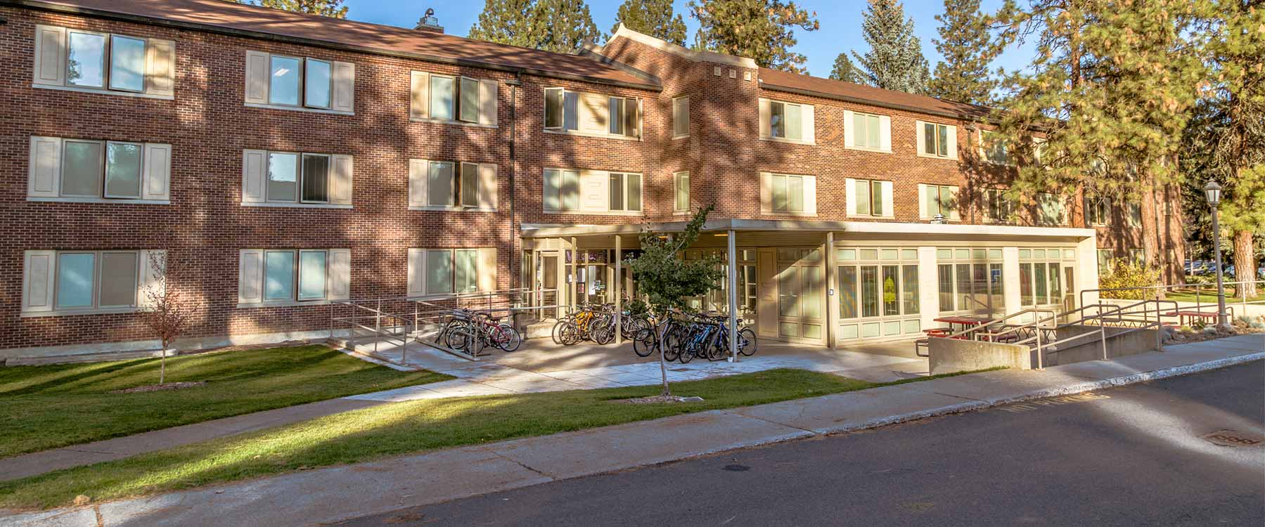 A three-story brick building with bikes out front, surrounded by a well-maintained lawn and trees.