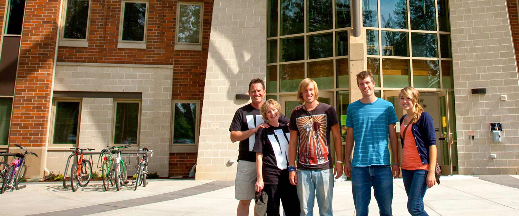 A family stands outside of a campus residence hall. They pose and smile.