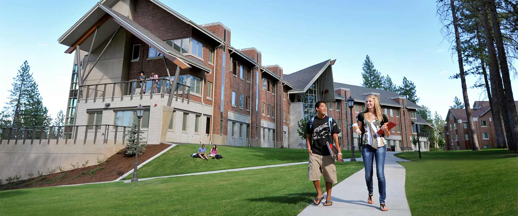 Two students walk on the path away from Oliver Hall, a large three-story brick residence hall.