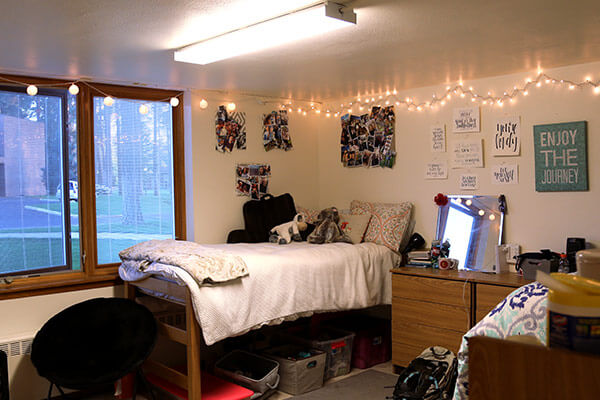 A student's dorm room with a lofted bed and twinkle lights.