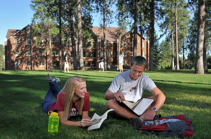 Two students lie in the grass outside of Duvall Hall. They have open books in front of them.