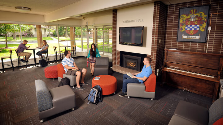 Students sit in large chairs around a fireplace in the common area of Stewart Hall.