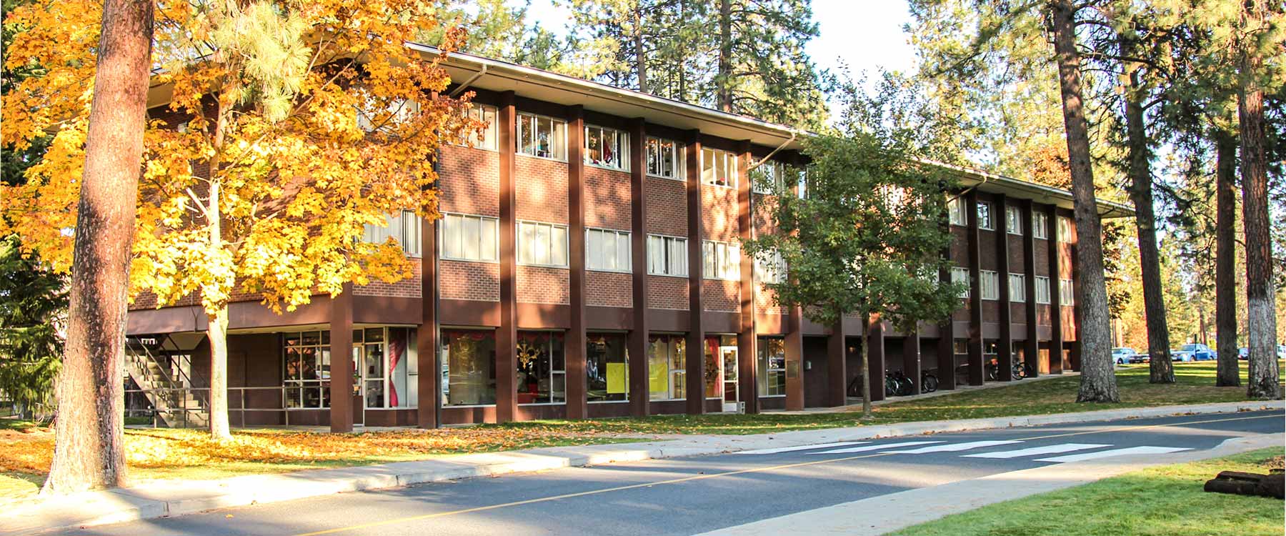 A large, rectangular three-story residence hall surrounded by autumn trees on a clear day.