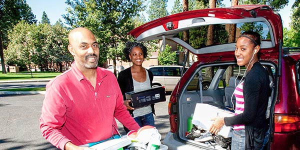 Two parents help their student unload belongings from the back of an SUV.