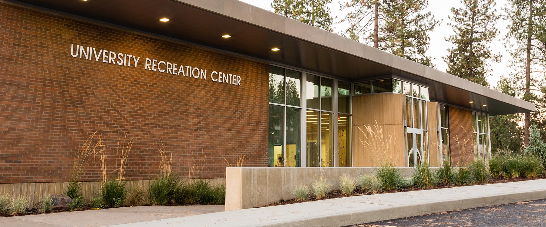 The exterior of the U-Rec building, a modern glass and brick building with a concrete railing and border of tall grasses.