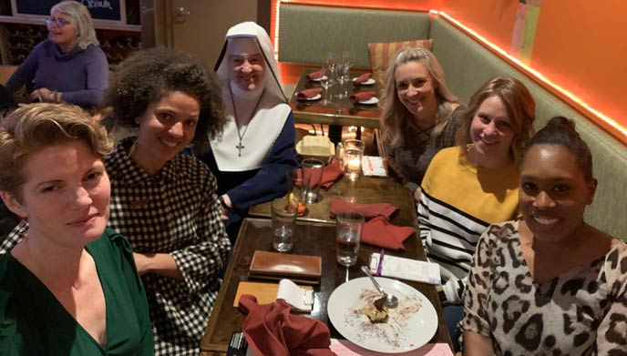 Six women, including a nun, smiling at a restaurant table with dessert.