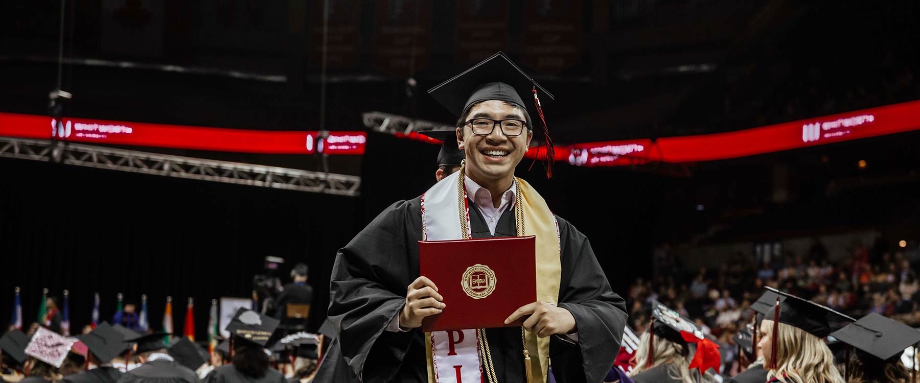 A student, wearing a cap and gown at commencement, smiles. 