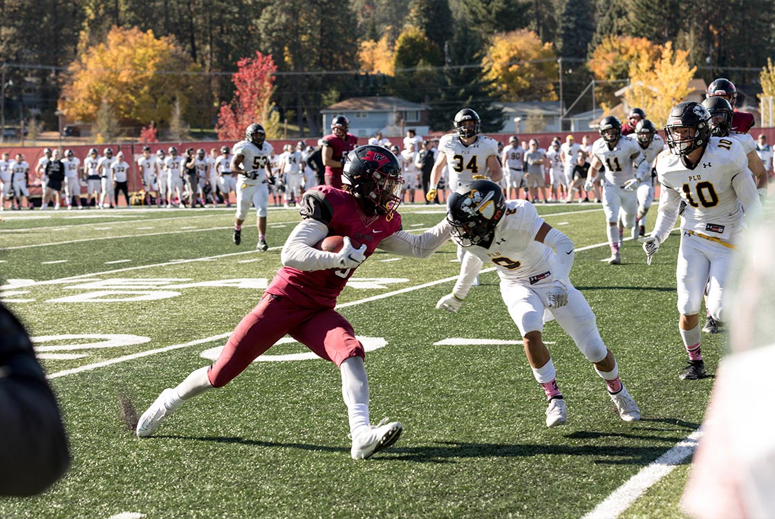 A football player in a red uniform evades a tackle from a player in a white uniform as others approach.