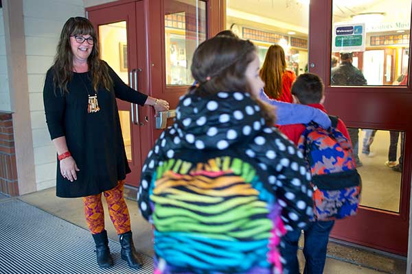 Amy holds a door open as a line of elementary students file inside.