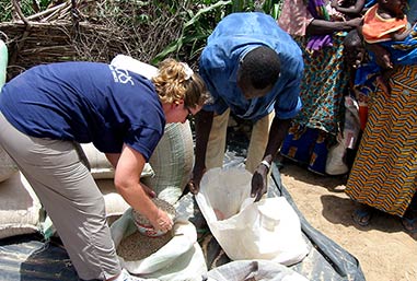 Anna bends over and scoops grains to distribute to nearby refugees. 