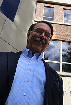 Arlin stands in front of a campus building and looks down smiling at the camera.