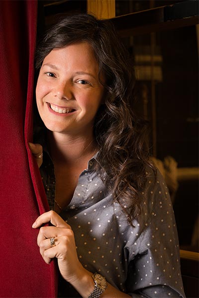 Brooke stands partially behind a red stage curtain and smiles.