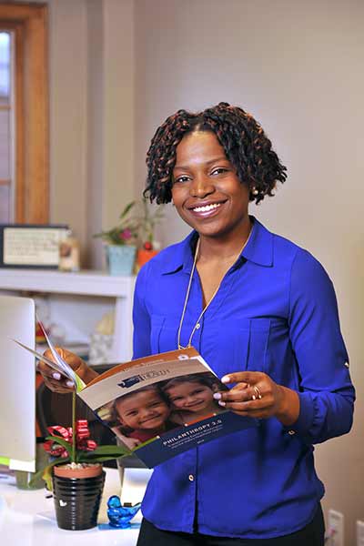 Christina stands in an office holding an open pamphlet. She poses and smiles.