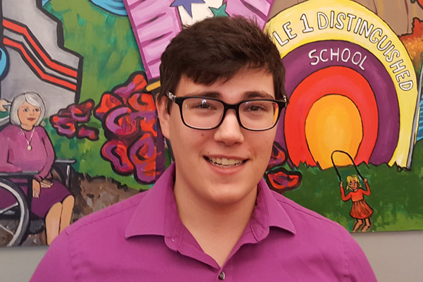 Daniel smiles in front of a large colorful mural.