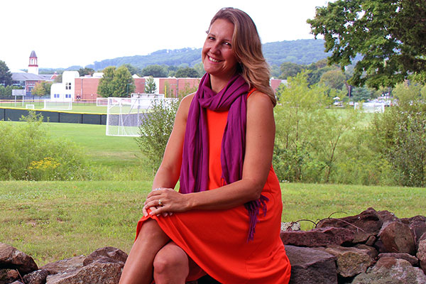 Diana sits outside and smiles. Behind her are school athletic fields.