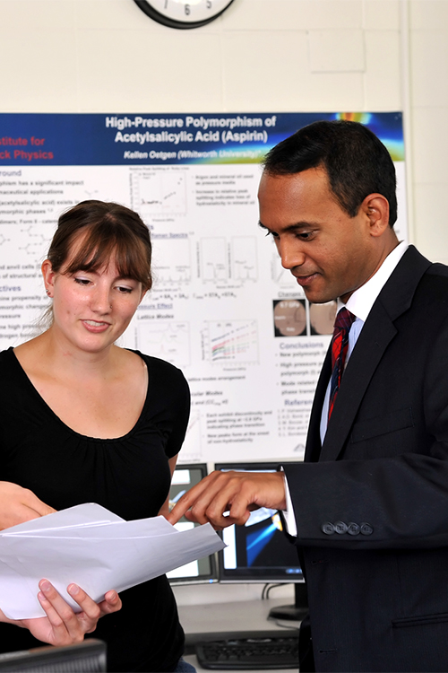 Kamesh stands speaking with a student. They examine a sheet of paper together.