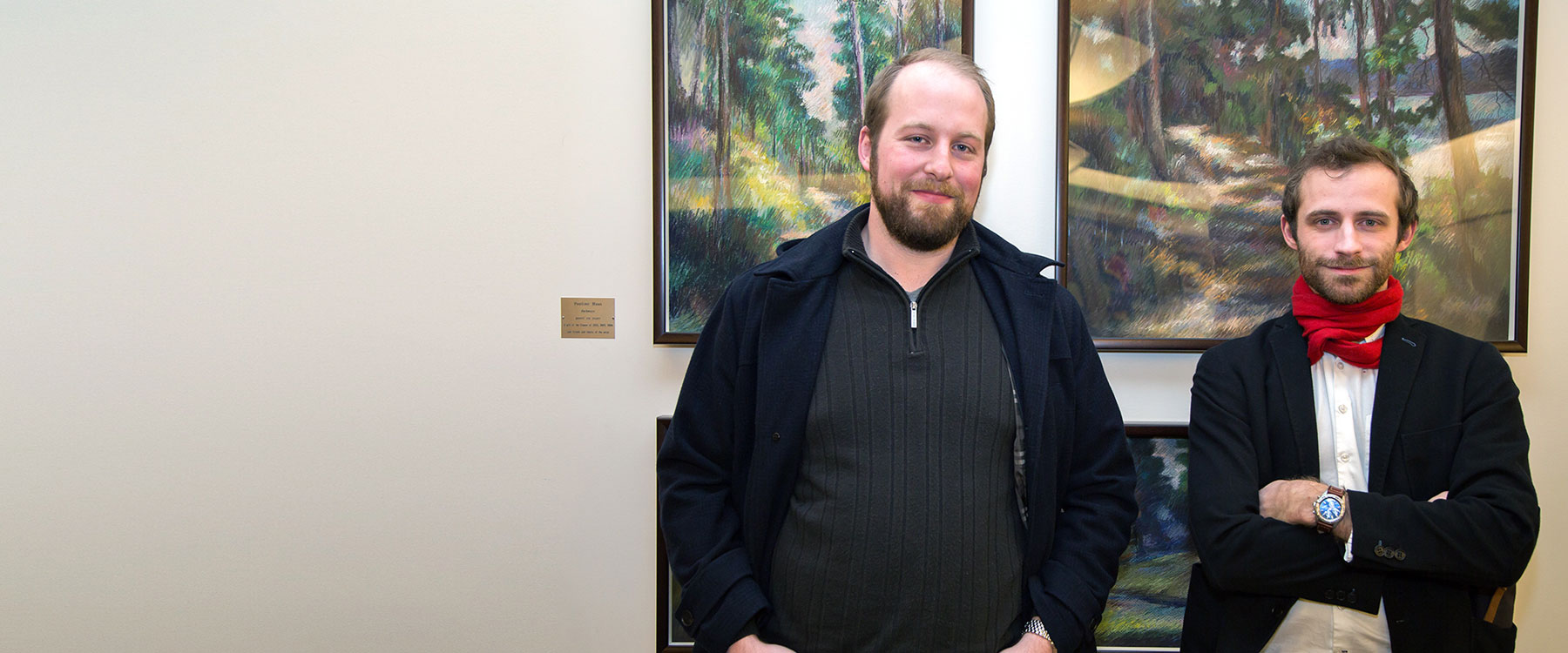 Kelly and Ryan stand together and smile with three forest artworks behind them.