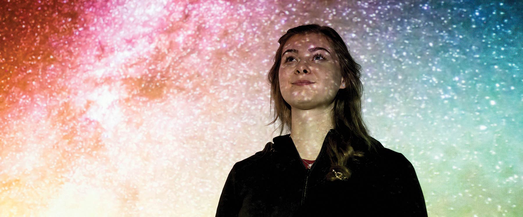 Maria Straight stands in front of a colorful backdrop of stars.
