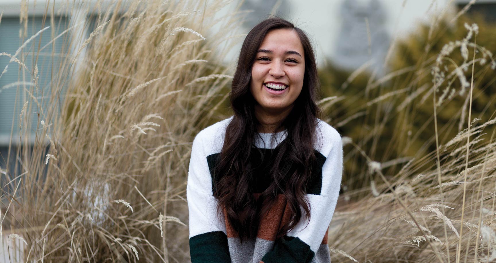 Megan Wynecoop sits outdoors among tall grasses and smiles.