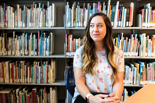 Nichole Clark sits in front of a book shelf and looks to the left smirking.