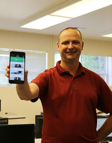 Pete Tucker holds up a phone with an app open and smiles.