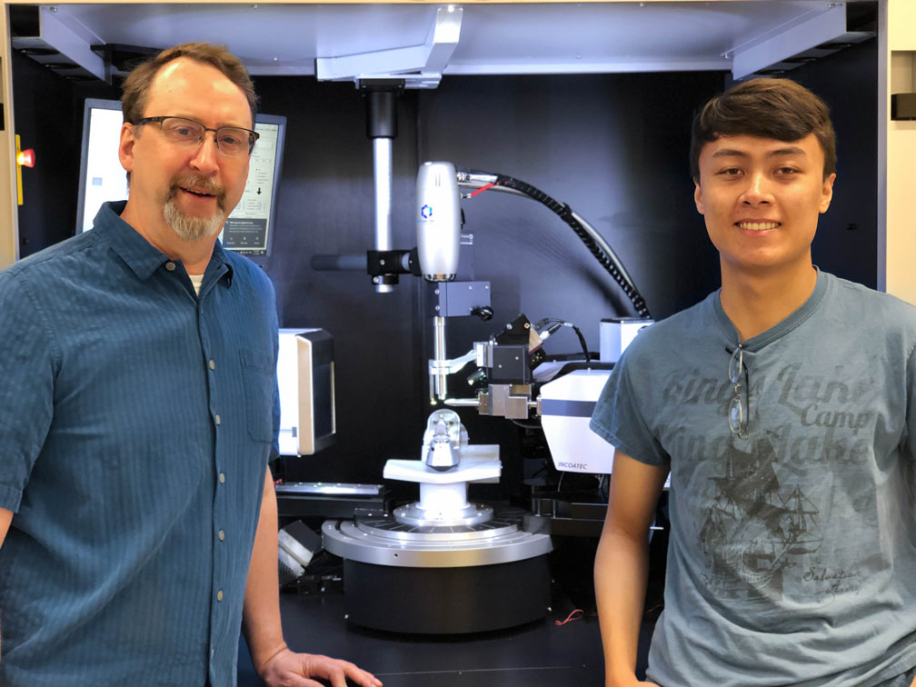 A student and instructor stand, smiling, near a high-tech machine in a lab.
