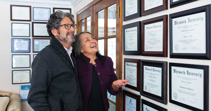 Two people looking at the wall with awards on it.