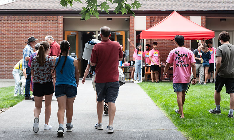 Students and parents walk toward a building and booths at an outdoor campus event.