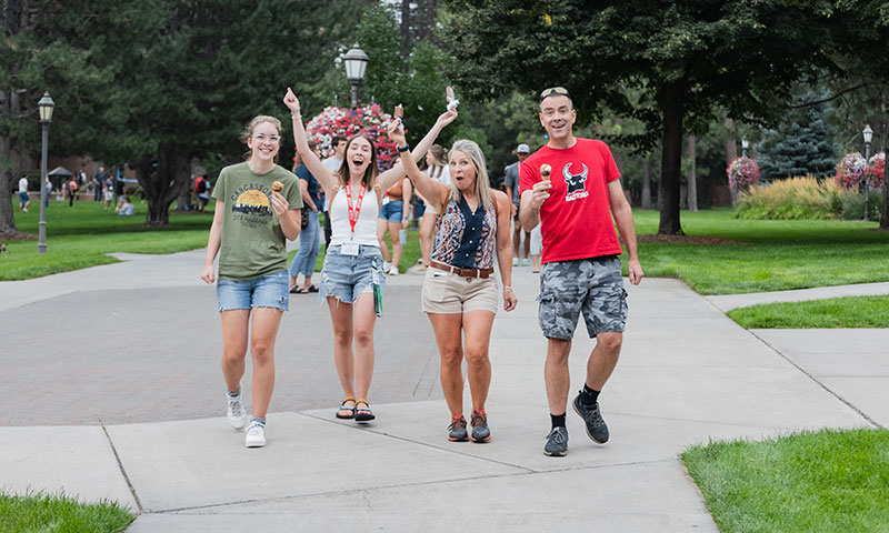 Two parents and two students walk together down a campus path, smiling and holding ice cream cones.