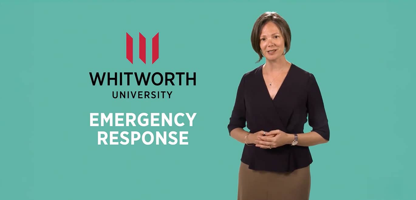 A Whitworth staff member stands, hands clasped, in front of emergency response graphic.