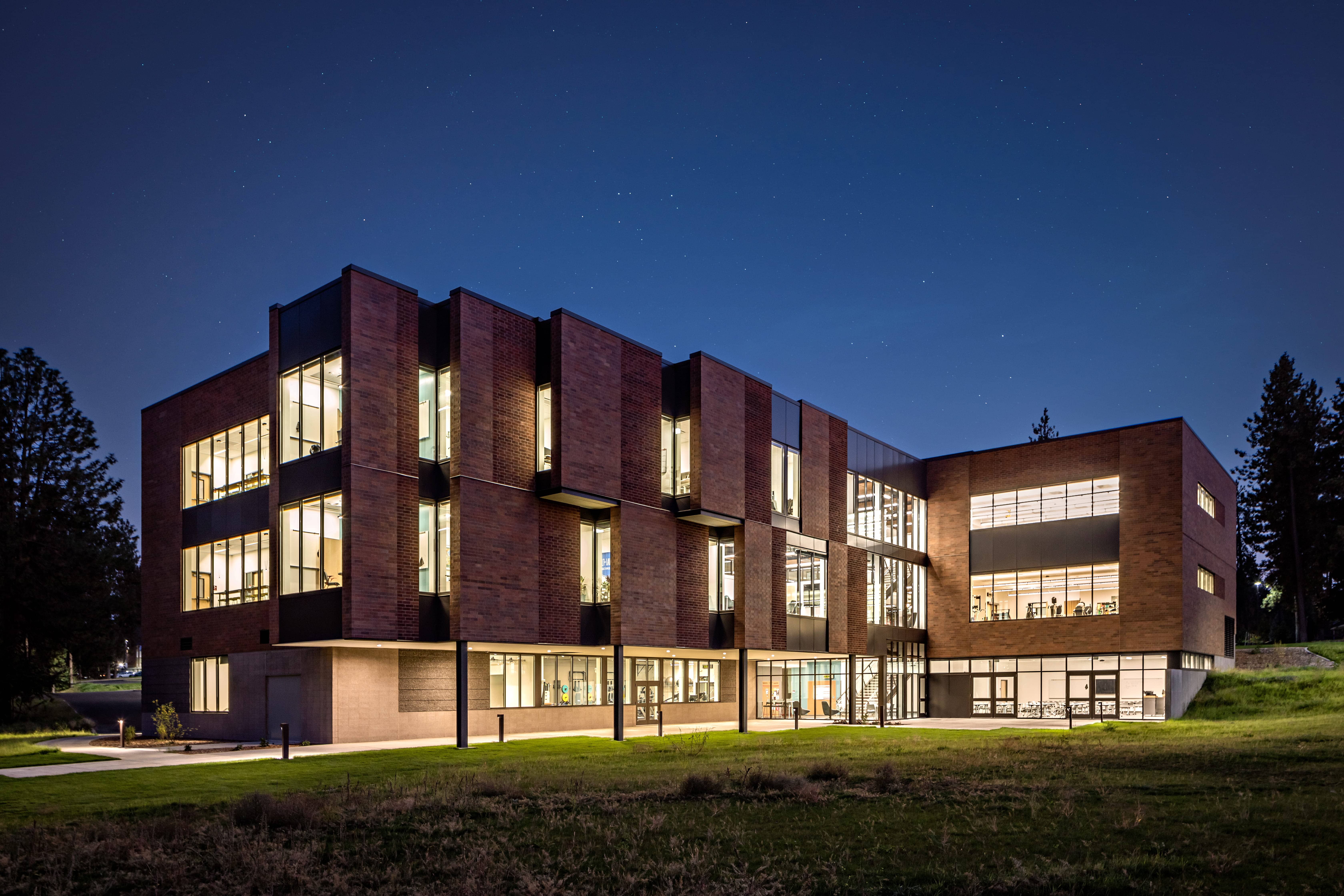 An academic building glows with many lit windows on a clear night.